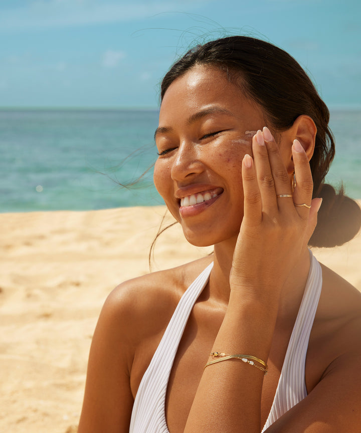 Woman enjoying the sun at the beach while applying Original Glow SPF 30 Sunscreen Face Lotion with Kakadu Plum, Sun Bum