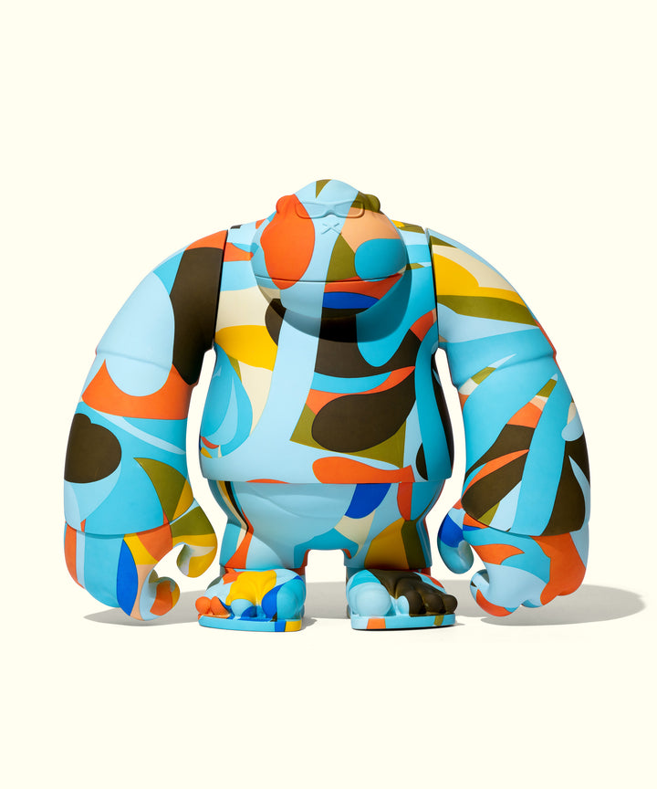 Colorful vinyl figurine with abstract geometric patterns in blue, orange, yellow, and green. Shaped like a rounded, stout character with short arms and legs. Playful and artistic design by Andy Davis for Sun Bum