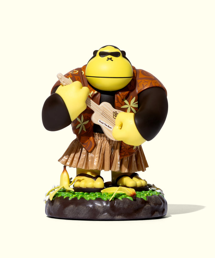 Hula Sonny figurine wearing a Hawaiian shirt and grass skirt, holding a ukulele on a tropical base. Escape to paradise with Sun Bum.