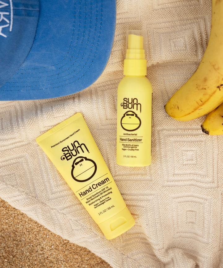 Original SPF 15 Sunscreen Hand Cream on a beach blanket with bananas and a blue hat, ideal for daily moisture and UV protection, Sun Bum.