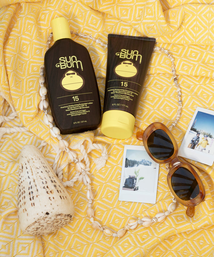 SPF 15 Sunscreen Lotion by Sun Bum, surrounded by summer accessories on a yellow patterned fabric.