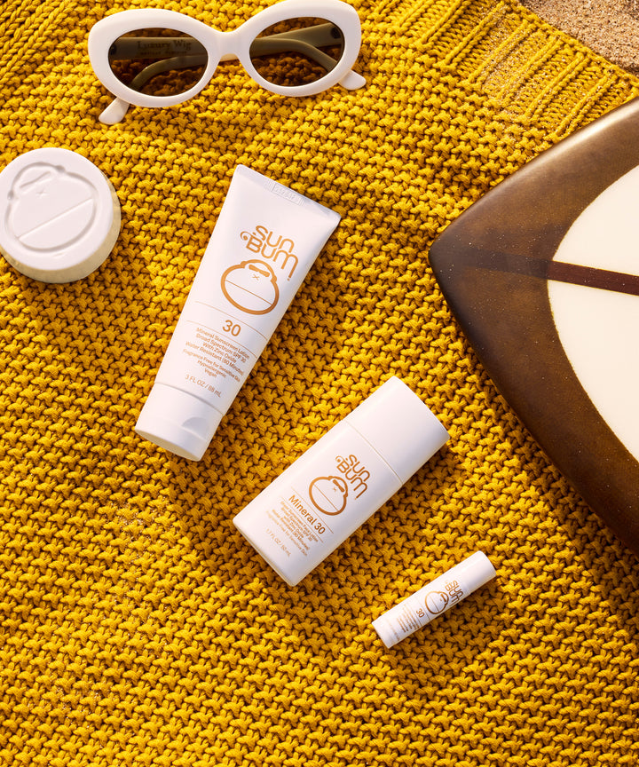 Mineral SPF 30 Sunscreen Lip Balm displayed on vibrant yellow knit textile alongside white sunglasses and other Sun Bum suncare products, showcasing zinc-based lip protection by Sun Bum